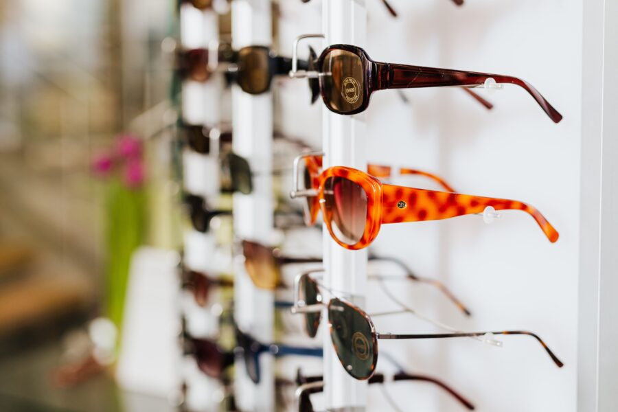 Sunglasses on a display rack in a store, focusing on brown tortoiseshell frames with various colors in the background